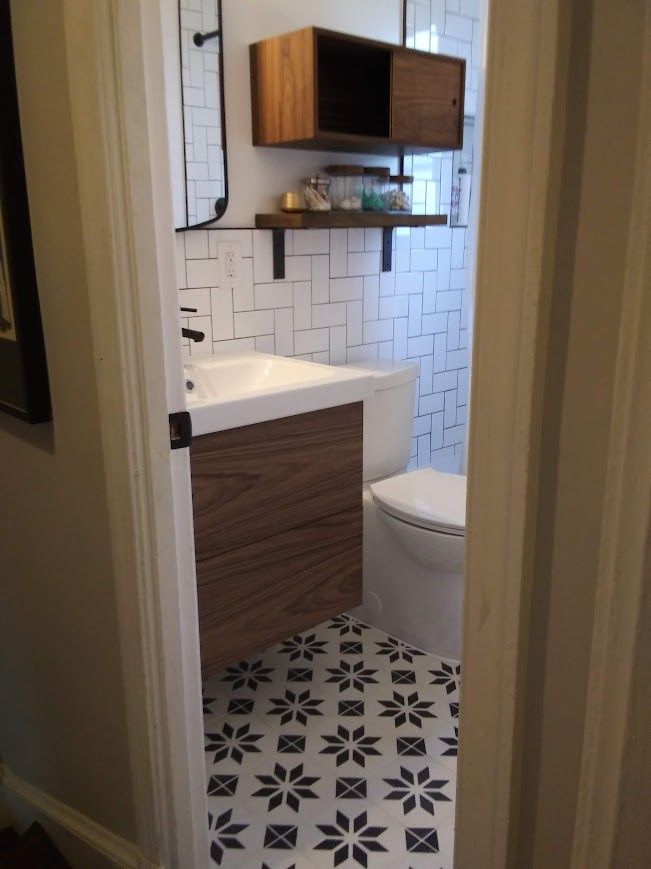 Bathroom with patterned floor, floating wood vanity, white tile, and storage cabinet.