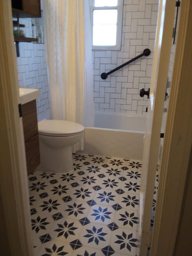 Bathroom with patterned floor, subway tile walls, toilet, and bathtub with grab bar.