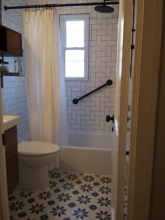 Small bathroom with patterned floor, white subway tile, and a grab bar by the tub.