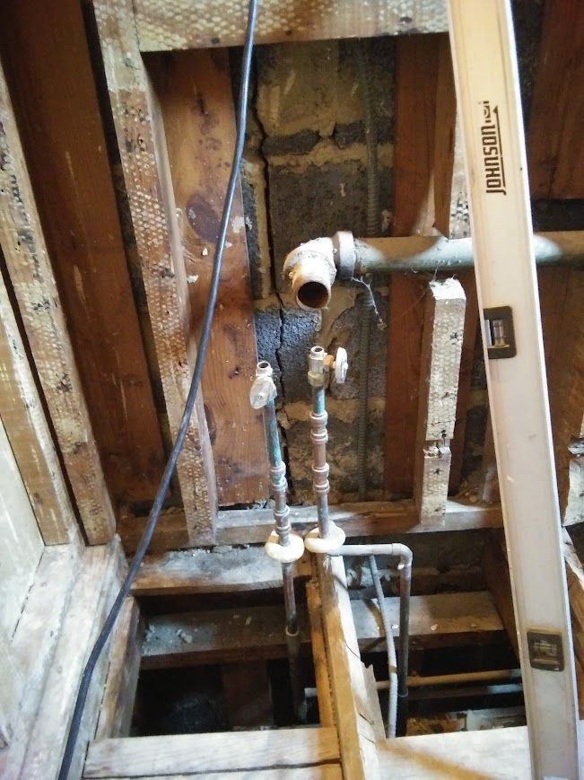 Wooden framing with plumbing pipes and valves. A level is visible.