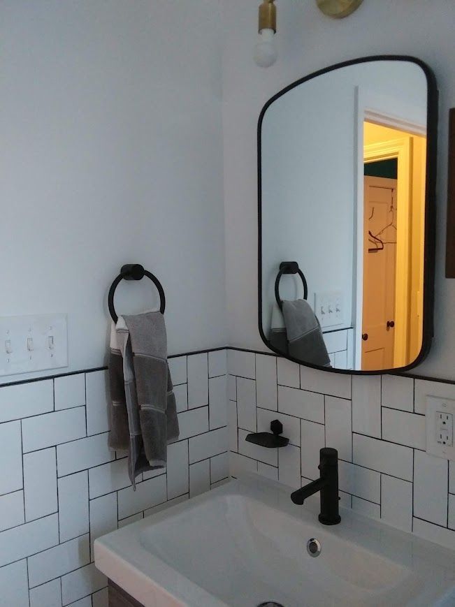 Bathroom with white and black tile, black fixtures, and a mirror. Towel hanging on a ring.