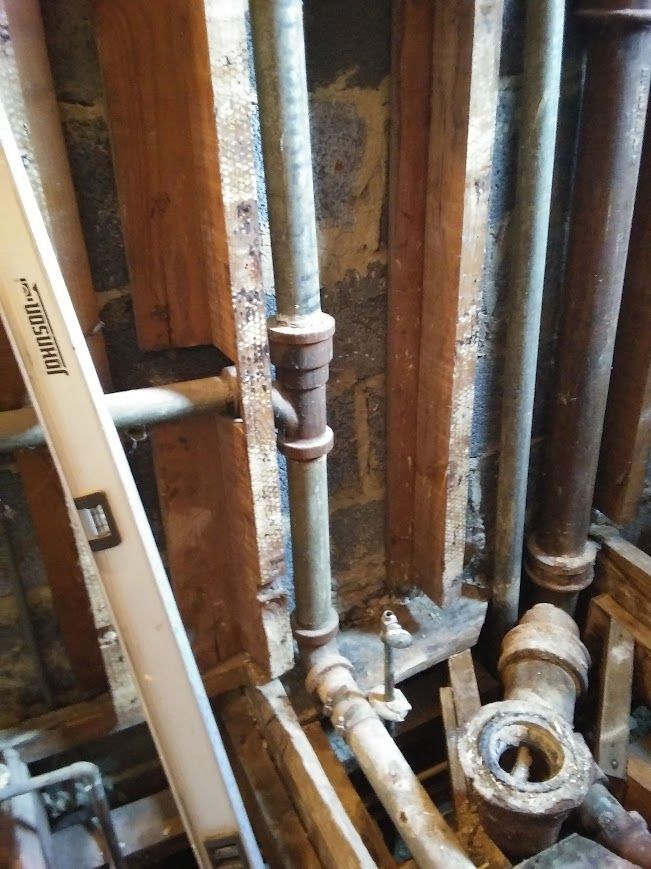 Pipes and wooden framing in a partially constructed wall.