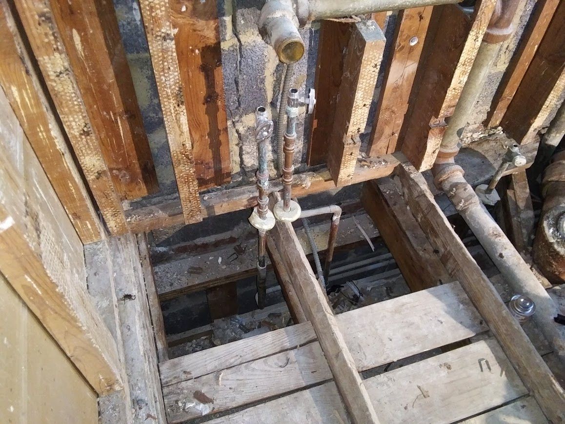 Open ceiling revealing wood beams, pipes, and plumbing fixtures.