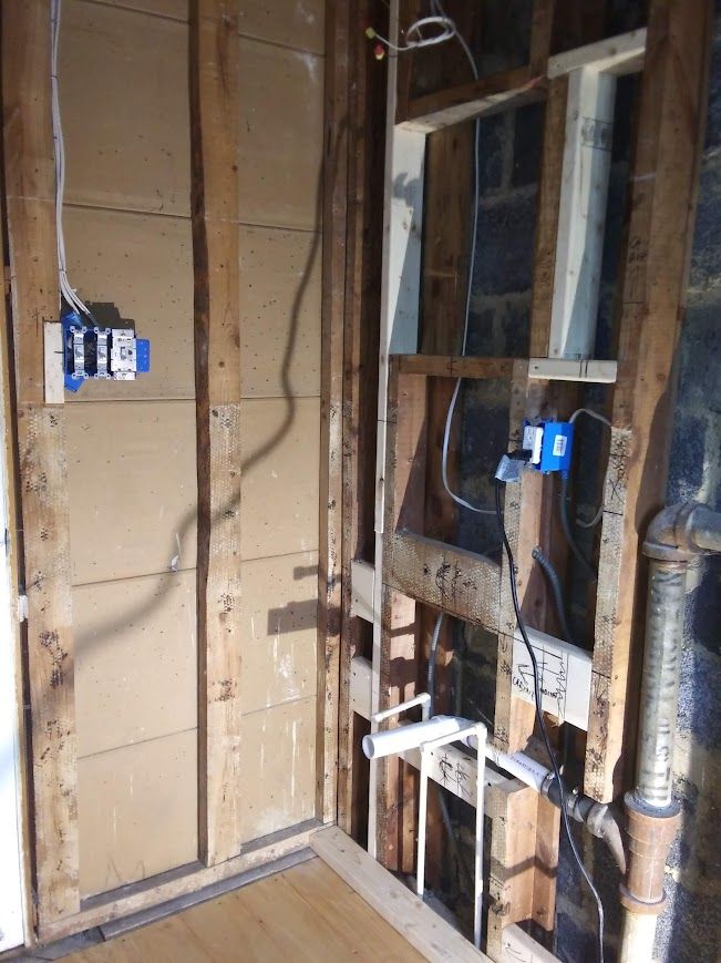 Exposed wall studs with electrical boxes, plumbing, and wiring in a room undergoing construction.