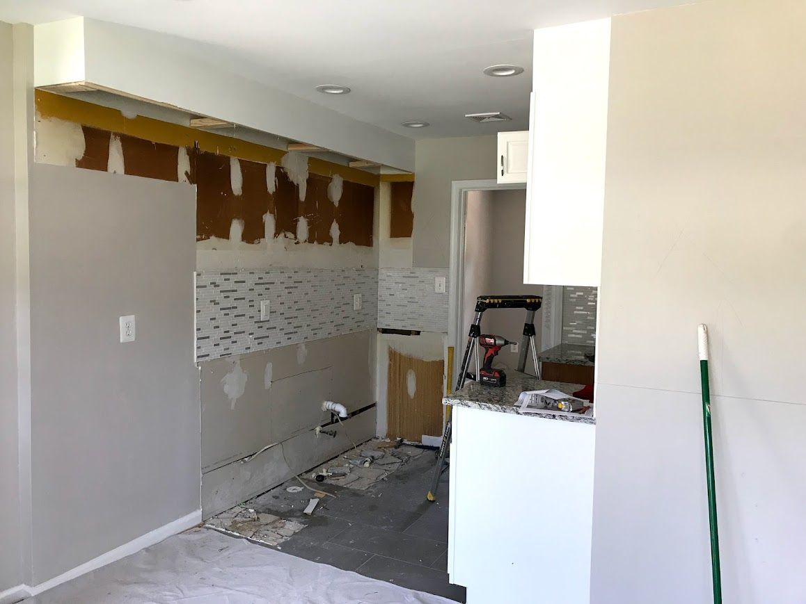Kitchen undergoing renovation, with exposed wall studs and tiling partially installed.
