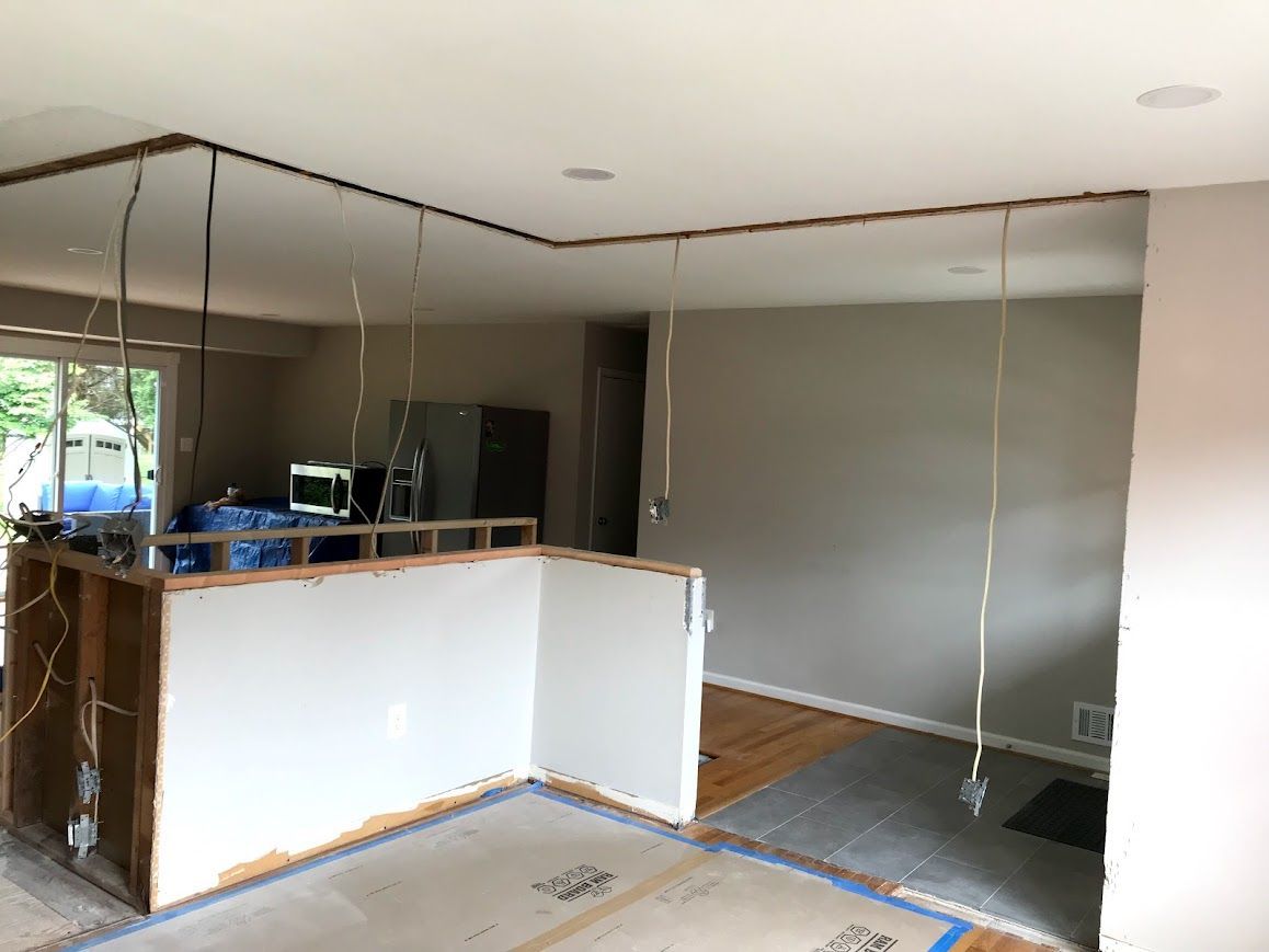 Kitchen undergoing renovation; exposed wiring, partially demolished walls, and ceiling framing visible.