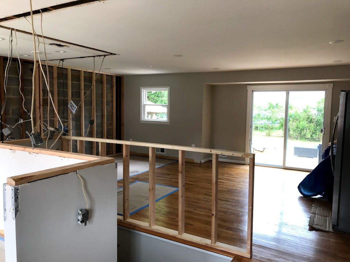 Interior renovation: Exposed wall studs, electrical wiring, partial drywall, wooden floors, sliding glass door, and window.
