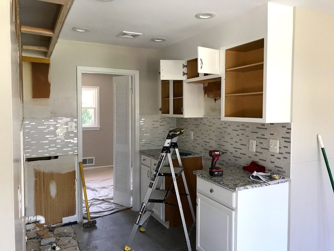 Kitchen under renovation: White cabinets, gray countertops, mosaic backsplash, ladder.