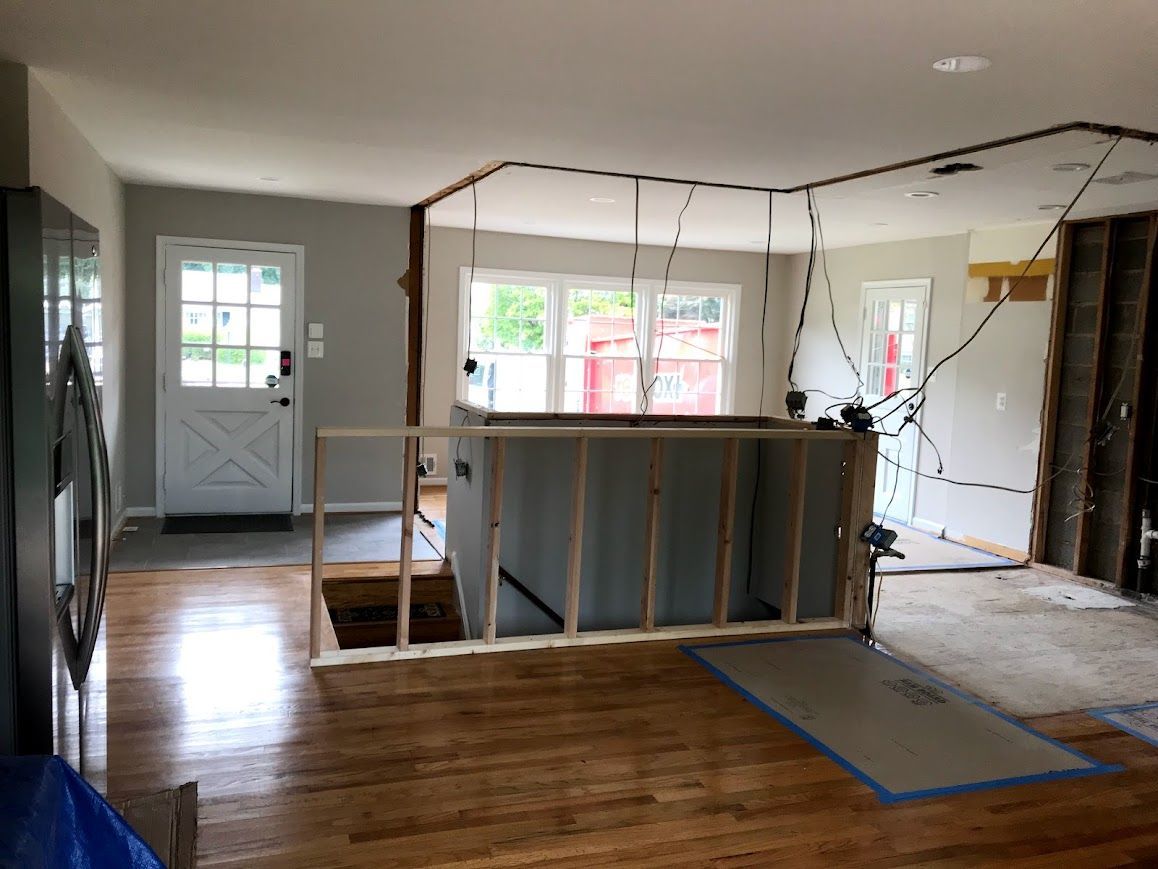 Interior view of a home undergoing renovation. Exposed studs, wiring, and partially demolished walls are visible.
