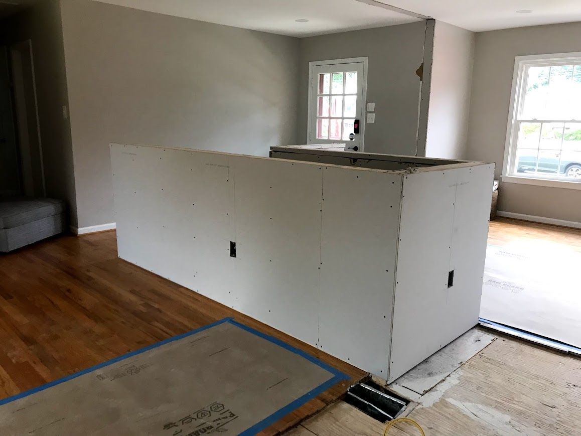 Drywall island under construction, hardwood floor, grey walls, open room, door, window.