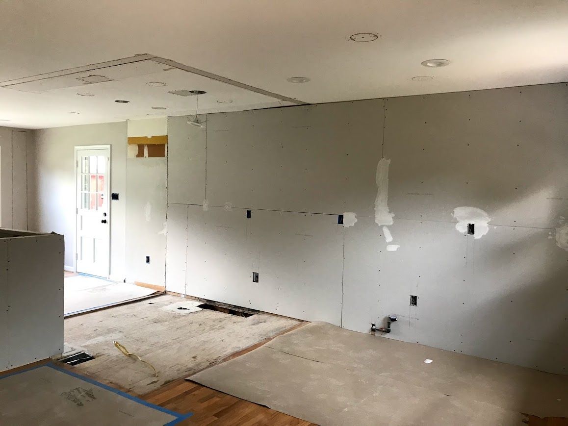 Interior renovation of a room with drywall installed on walls and ceiling; electrical outlets visible.