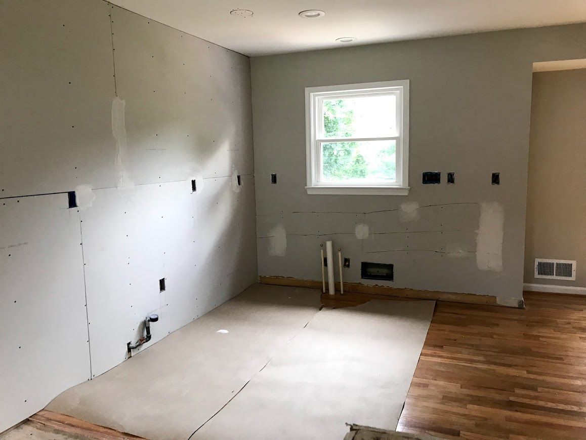 Interior of a room under renovation; drywall, window, plumbing, unfinished floor, and wood floor.