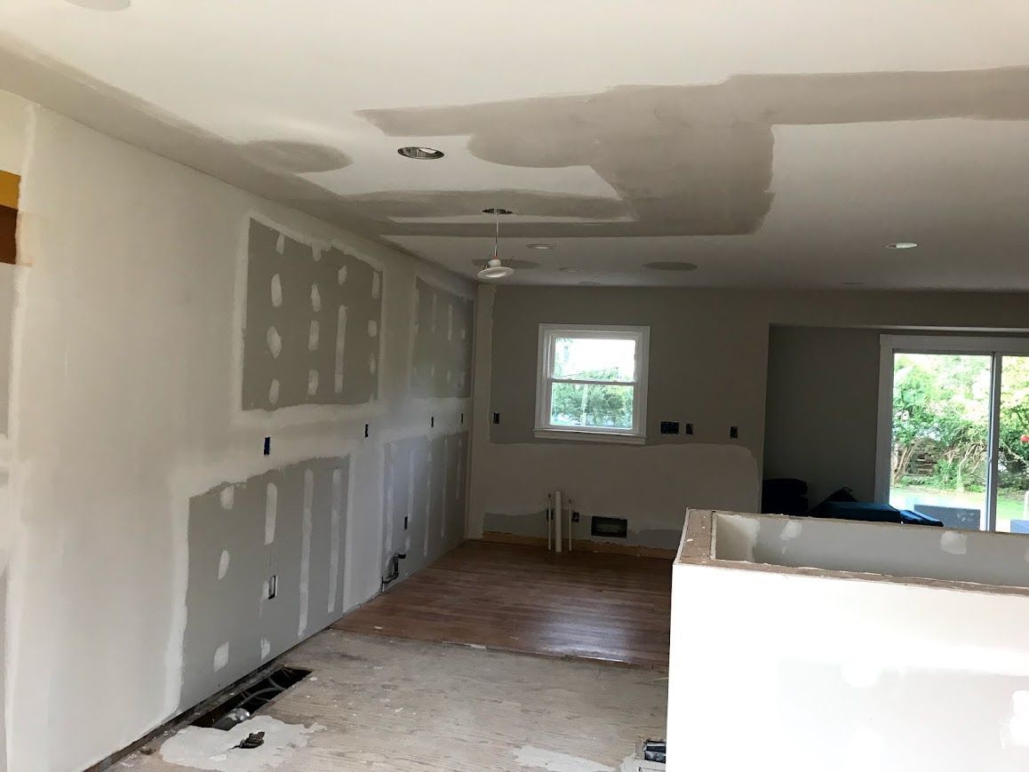 Kitchen renovation: drywall installed on walls and ceiling. Unfinished floors, window and sliding door visible.