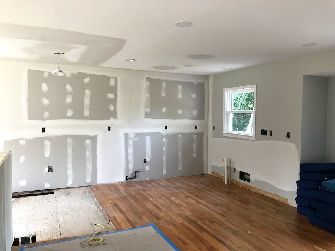 Interior of a room under renovation with drywall partially installed, hardwood floors, and a window.