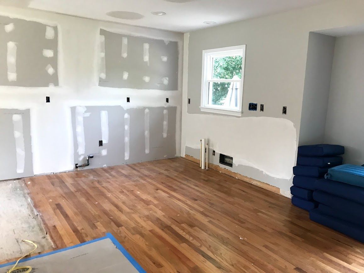 Room with hardwood floor and unfinished drywall; electrical outlets visible.