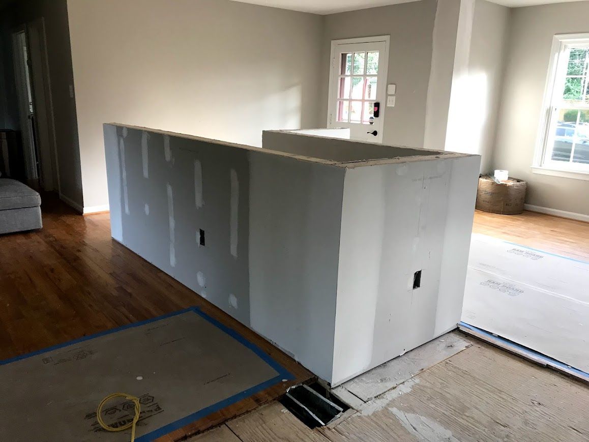 Drywall island under construction in a room, with wood flooring and window.