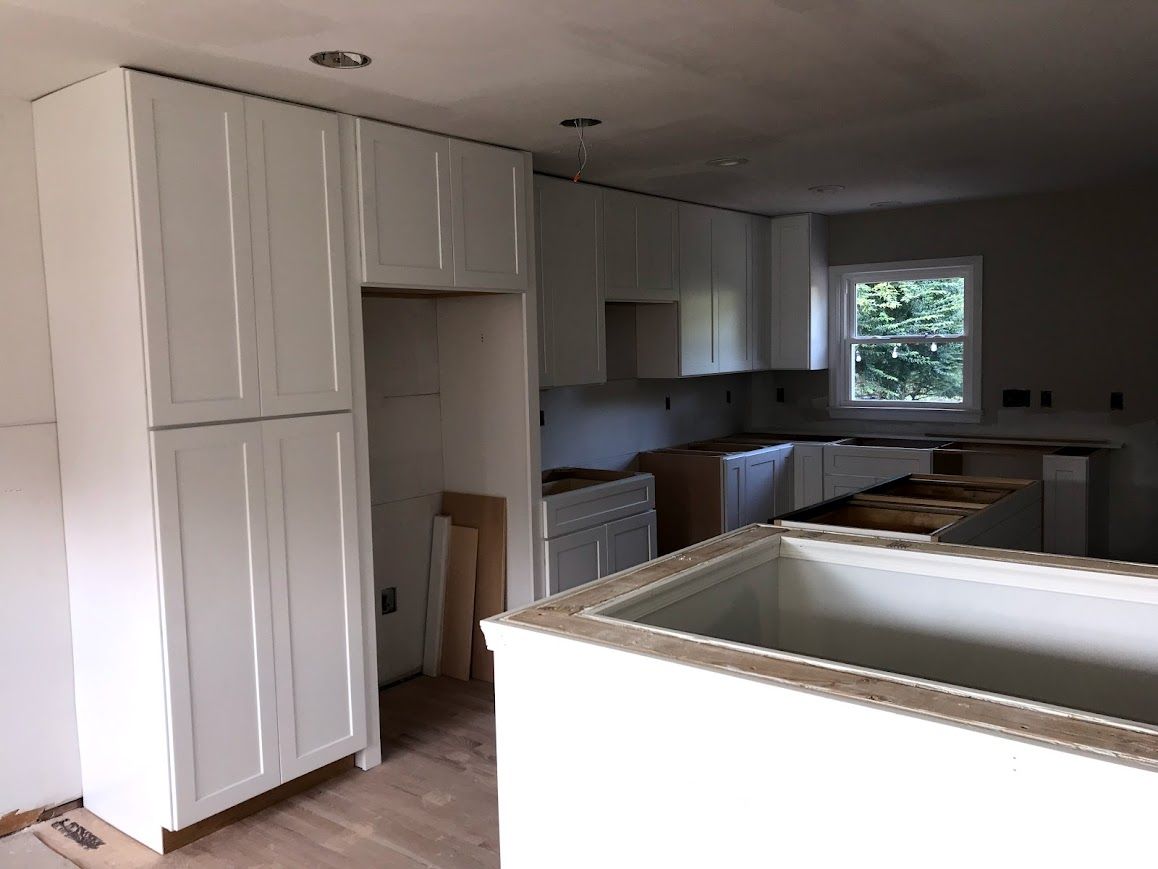 Kitchen under construction, white cabinets, unfinished island, window.