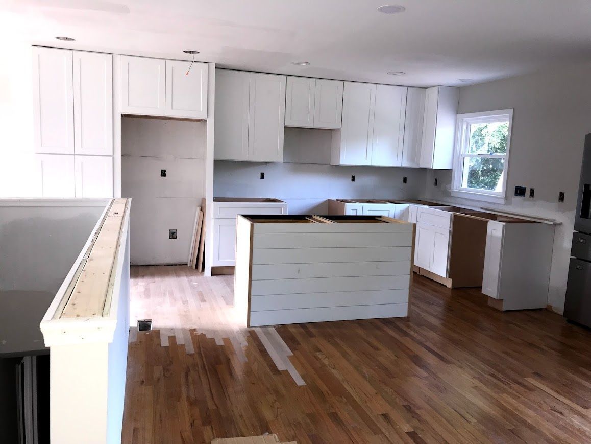Kitchen under construction with white cabinets, island, and wood flooring.