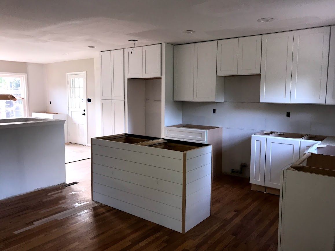 Kitchen under construction with white cabinets, island, and wood floors.