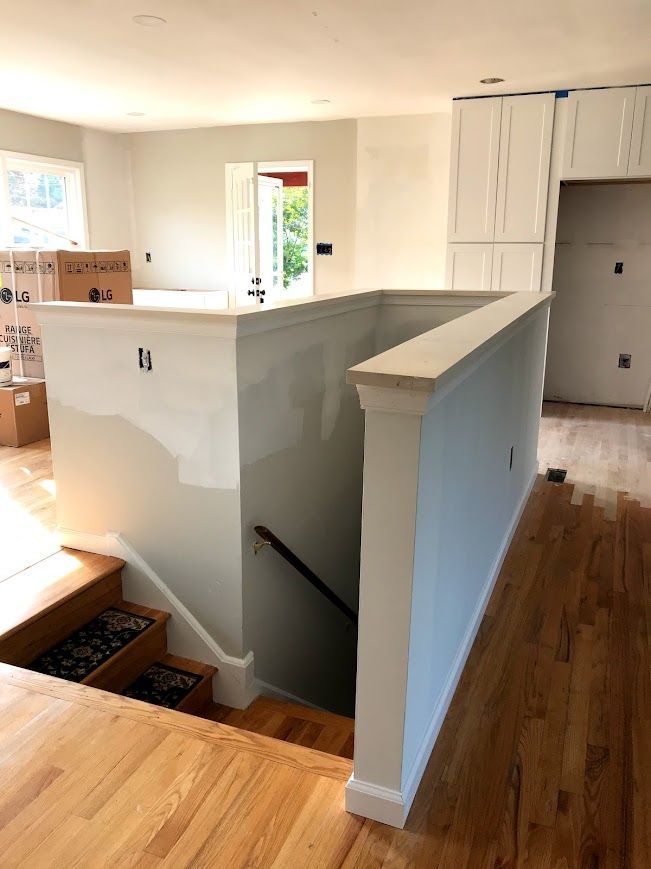 Interior view of a staircase and partial wall, hardwood floors, unfinished cabinets, and doorway to outside.