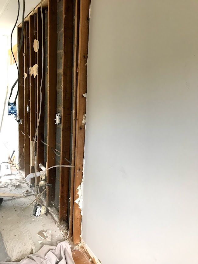 Interior wall under construction showing exposed wood studs and wiring, with a finished gray wall section.