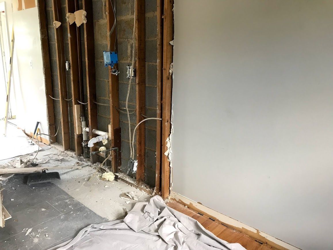 Interior wall under construction; exposed studs, electrical wiring, and a partially painted grey wall.