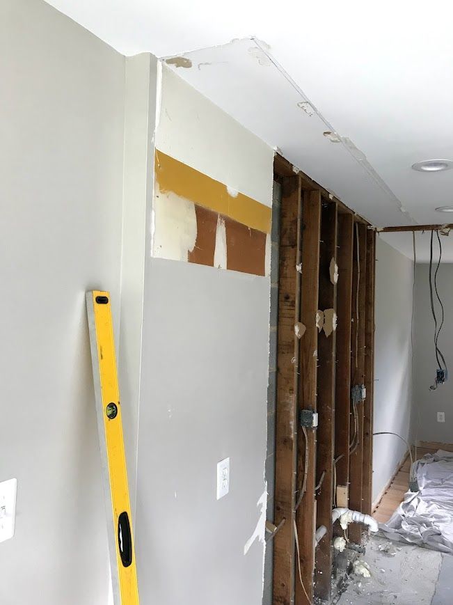 Wall undergoing renovation; exposed wooden studs, drywall partially removed, yellow level leaned against painted wall.