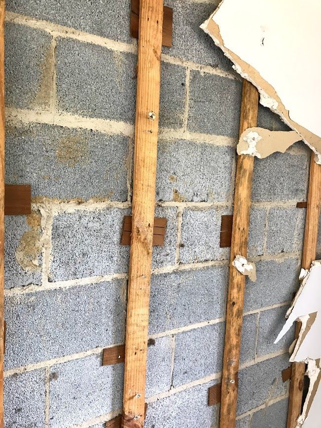 Exposed cinder block wall with wooden studs and ripped drywall.