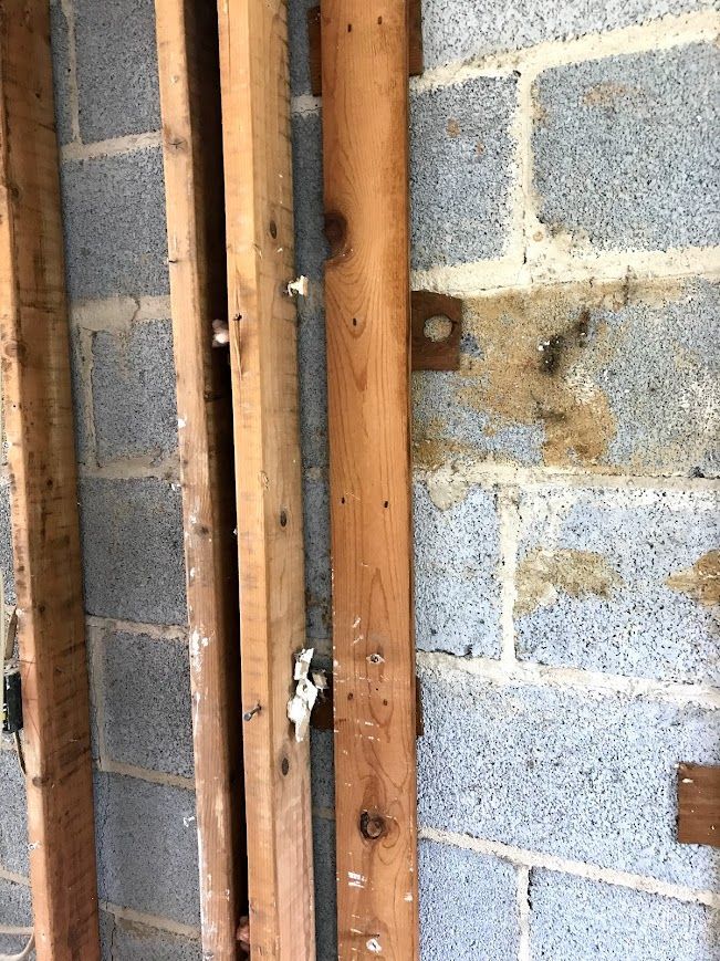 Wooden framing and metal bracket against a gray cinder block wall.