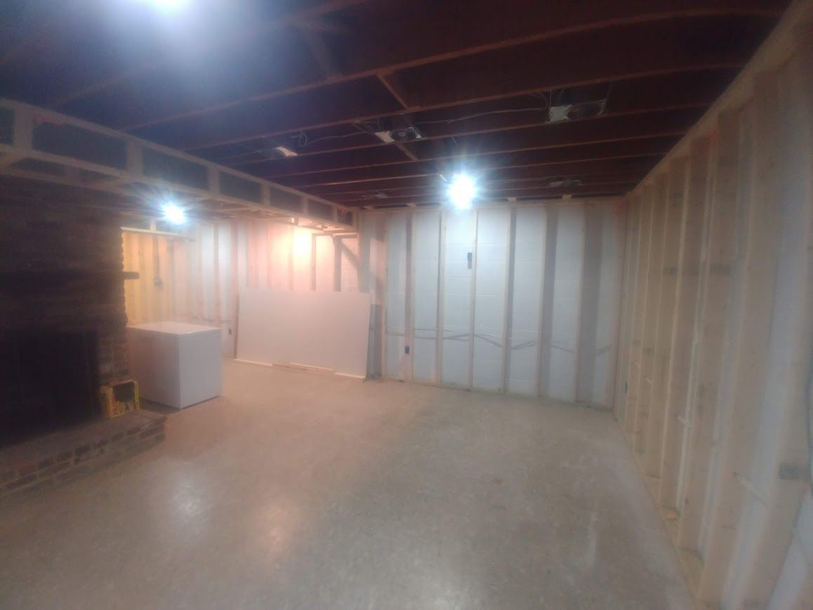 Unfinished basement with wood framing. Concrete floor, exposed ceiling joists, and a white appliance.