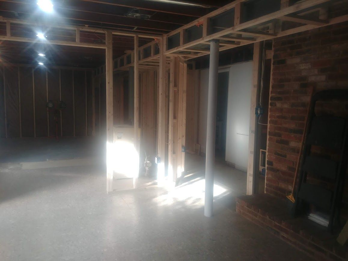 Interior framing of a room under construction. Visible wooden studs, brick wall, and a partially open door.