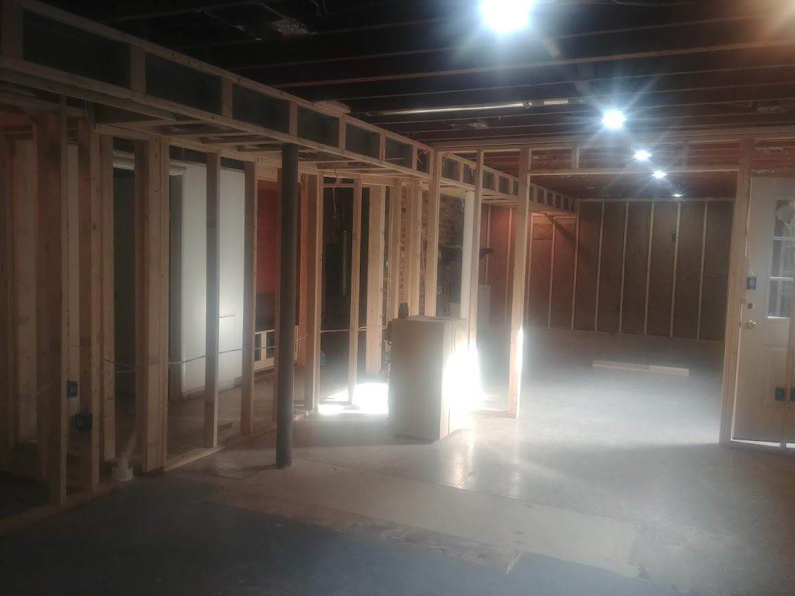 Unfinished basement with wooden framing for walls and doorways, dimly lit with overhead lights.