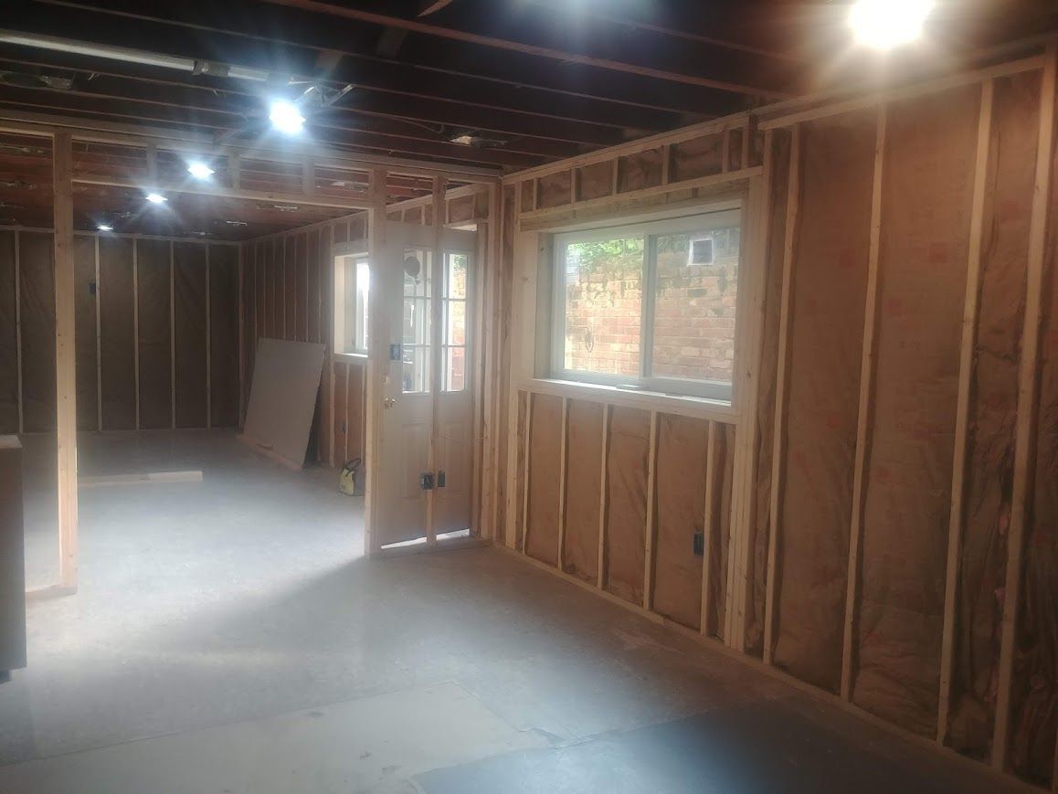 Interior of a room under construction, with wooden studs, a window, door, and exposed ceiling.