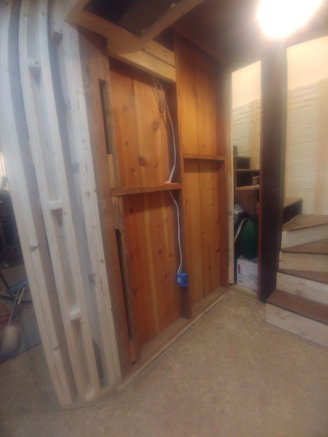 Interior space with wood-paneled wall, electrical wires, and steps to the right.