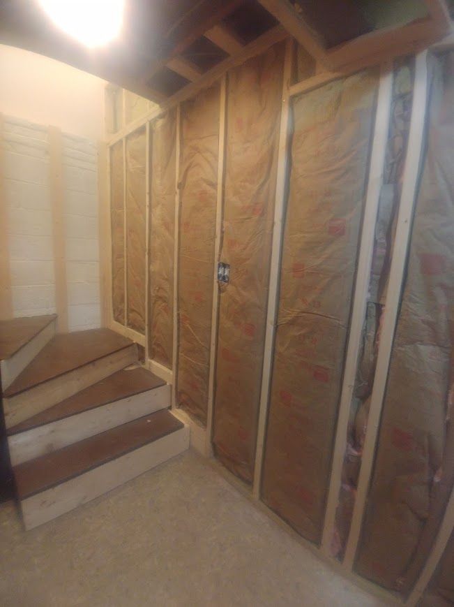 Stairway with wood steps next to framed, insulated walls. Electrical outlet visible.