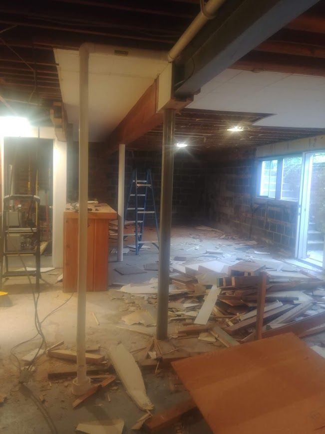 Basement under renovation with exposed beams, support columns, debris, and a ladder.