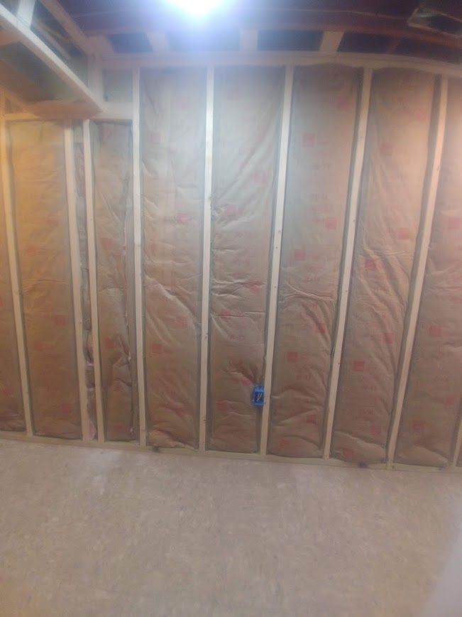 Interior wall framing with insulation between wooden studs, electrical box visible.
