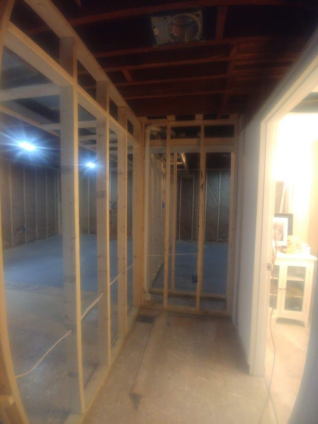 Wooden wall framing in a basement during construction. Studs and open doorways are visible, with a concrete floor.