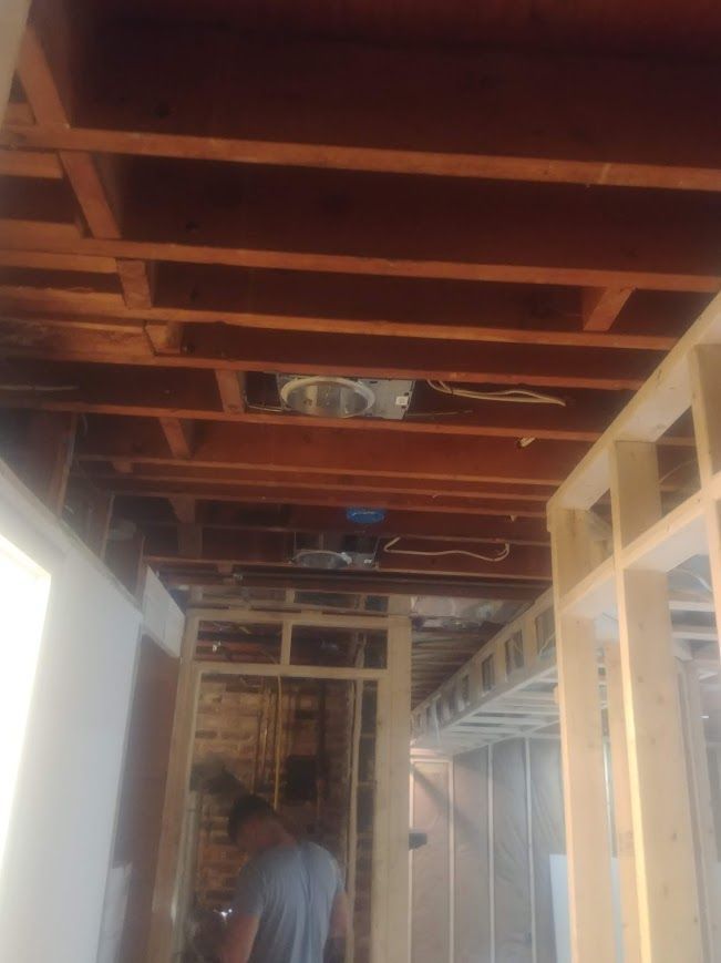 Construction site, exposed ceiling beams, electrical wiring, new framing, person in blue shirt.