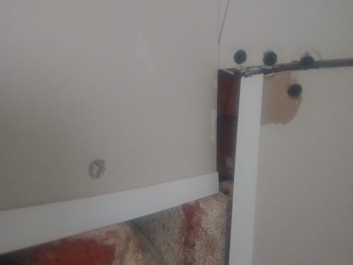 White drywall panels meeting at an inside corner, revealing brick. A white trim piece is visible.