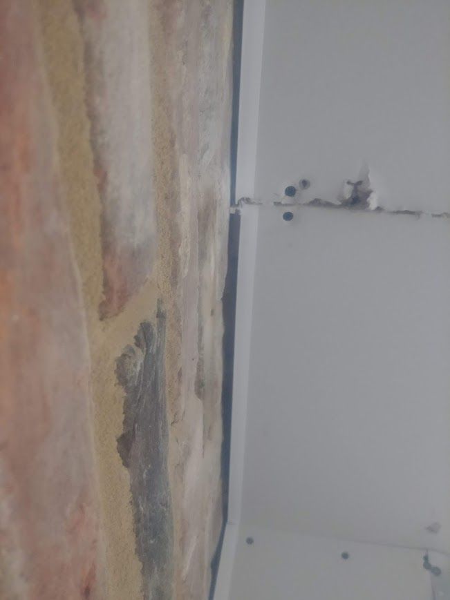 Close-up view of a brick wall beside a white wall with a black line in the middle.