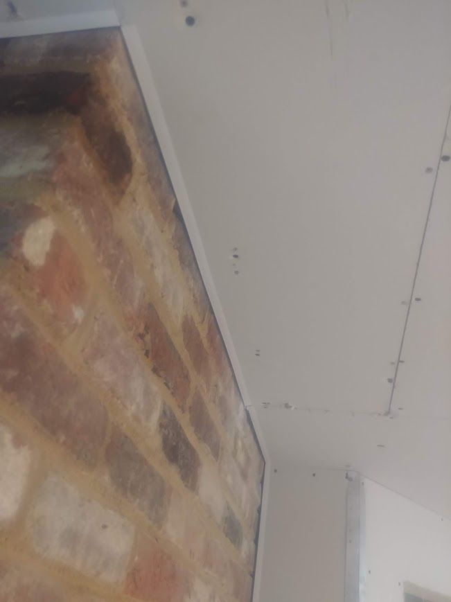 Brick wall meets white drywall at a corner, with metal trim.