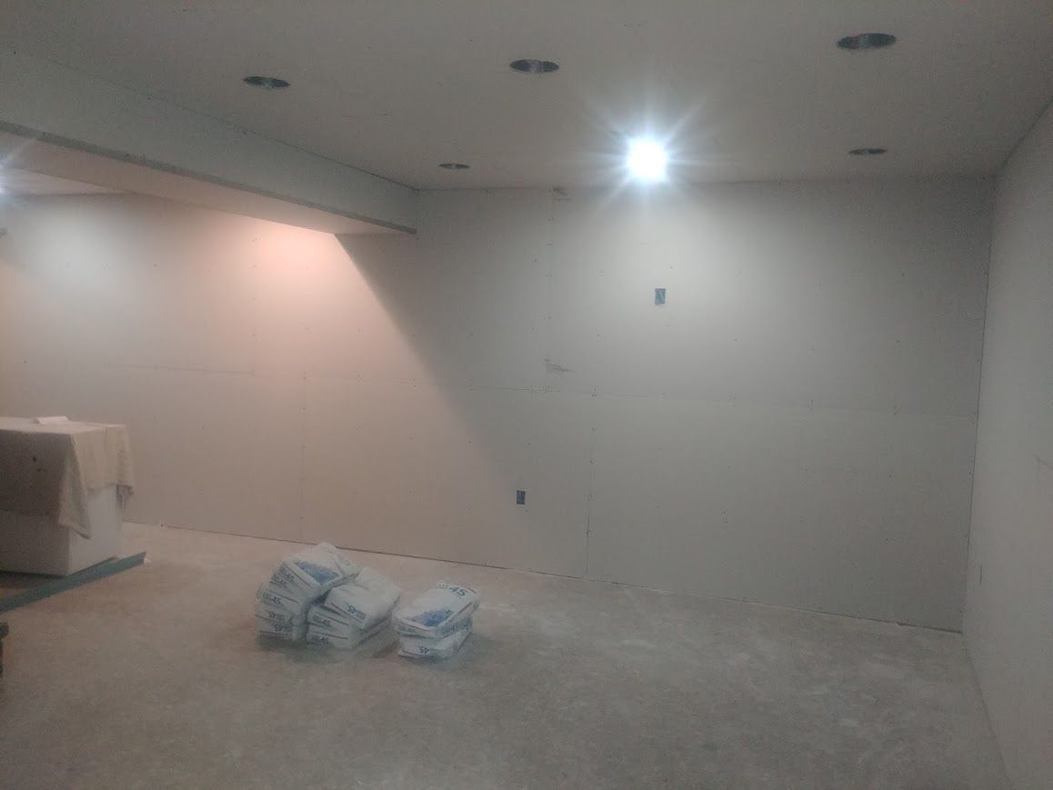 Empty room with drywall walls and ceiling, recessed lights, bags on floor.