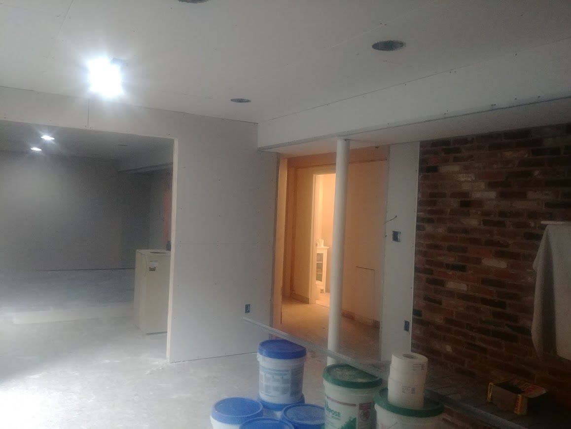 Interior of a room under construction with drywall and brick. Paint buckets are visible on the floor.