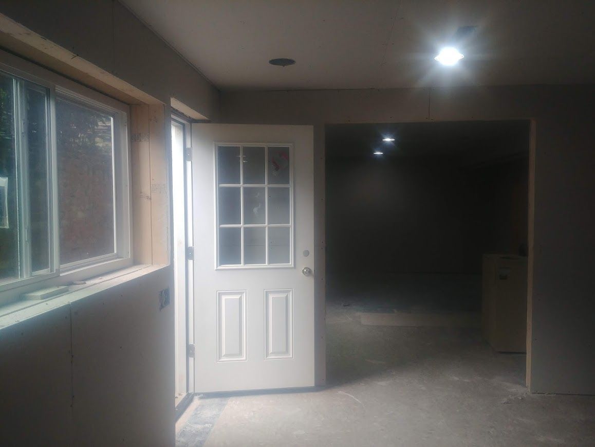 Open white door leading to a dark room. Interior view with a window, white walls, and a recessed ceiling light.