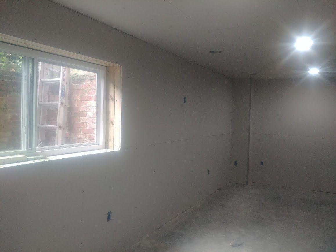 A room with gray walls, a window, and recessed ceiling lights. Unfinished floor.