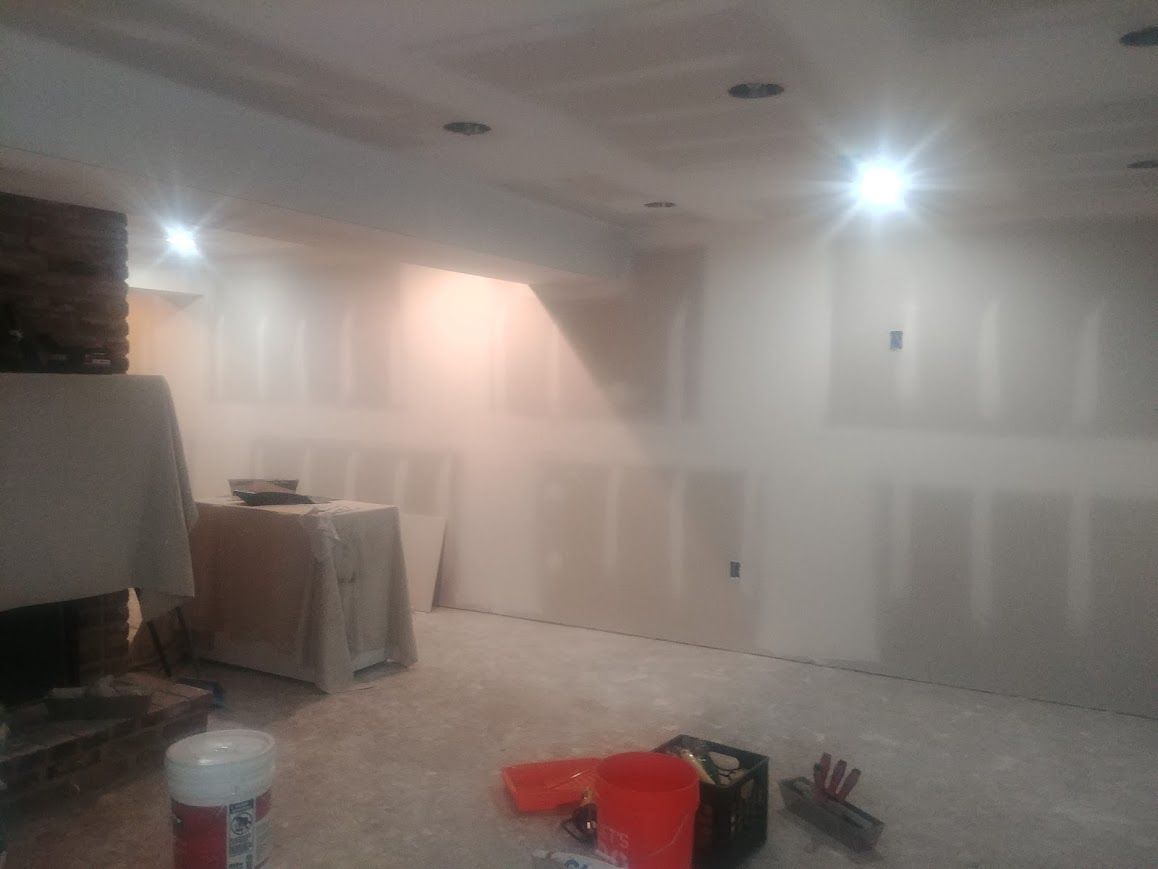 Room under construction, drywall installed on walls and ceiling. Tools and dust present.