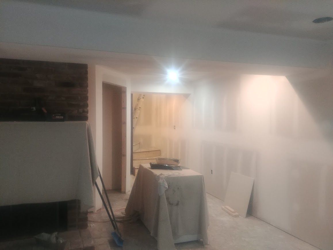Interior view of a room under construction with white drywall, a doorway, and a table covered in a sheet.