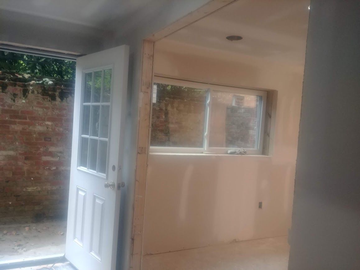 Interior view of a room with a white door and window. Drywall and unfinished walls are visible.