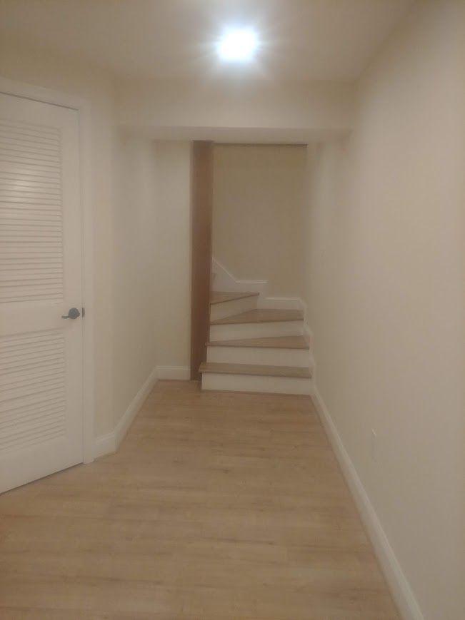 A narrow hallway with a door, stairs, and light-colored walls and flooring.